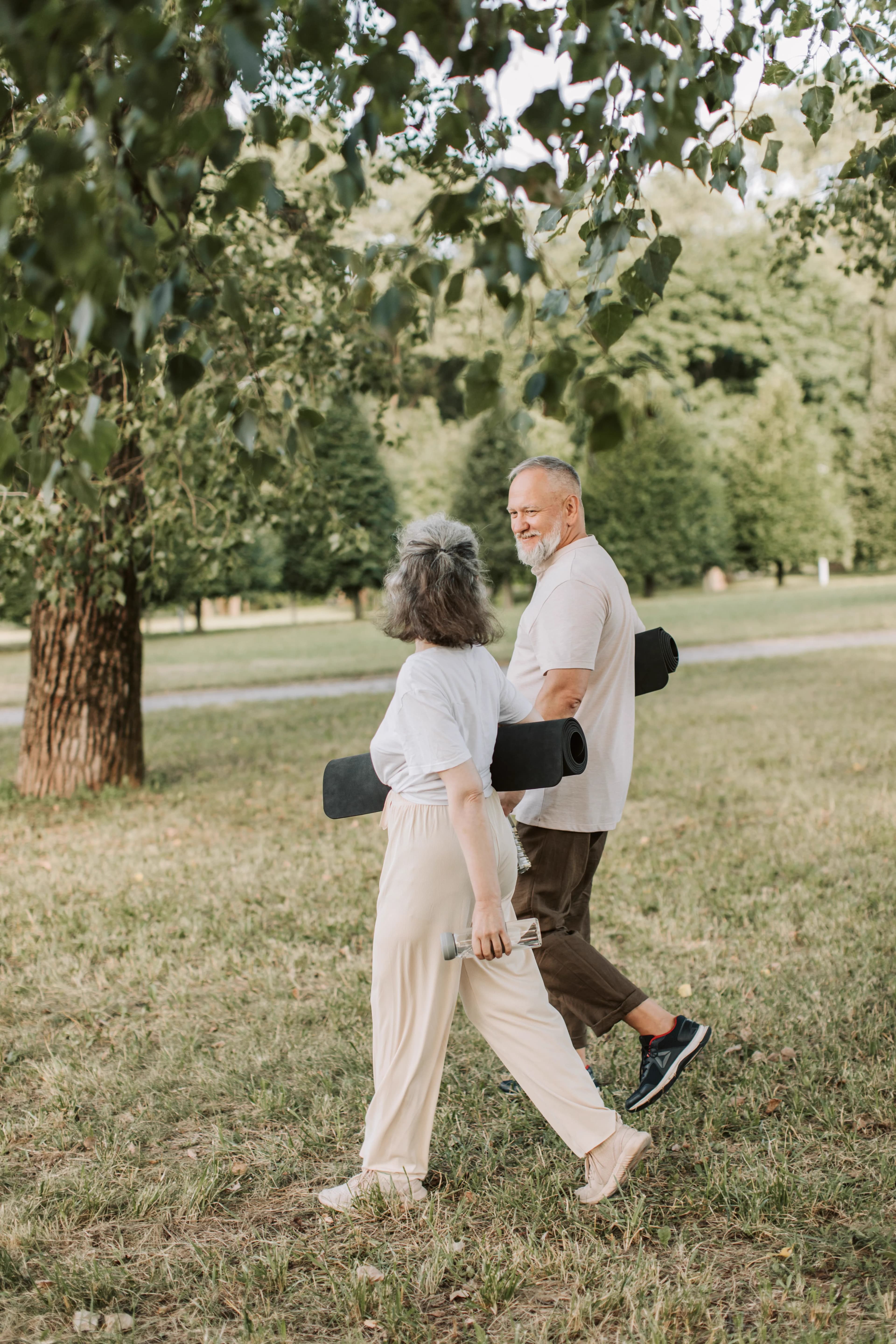 Two adults walking outdoors with exercise mats and a water bottle